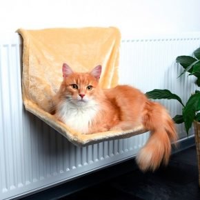рыжий кот лежит в светлом плюшевом гамаке, подвешенном на пластинчатом радиаторе отопления